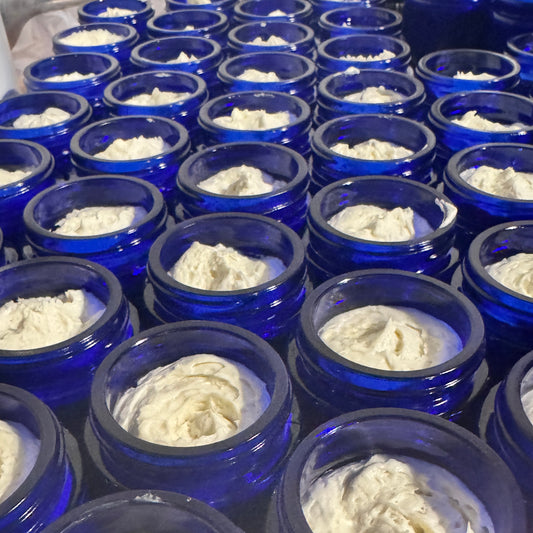 Multiple small blue glass jars filled with white pearl face cream, arranged closely together.